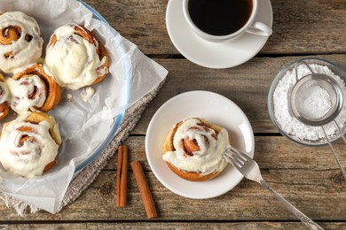 Tasty cinnamon rolls with cream served on wooden table, flat lay