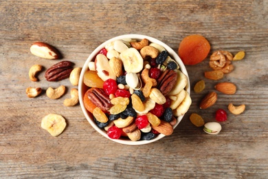 Bowl with different dried fruits and nuts on wooden background, top view.