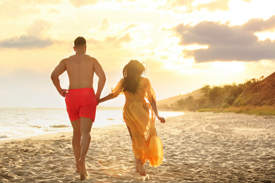 Photo of Lovely couple running together on beach at sunset, back view