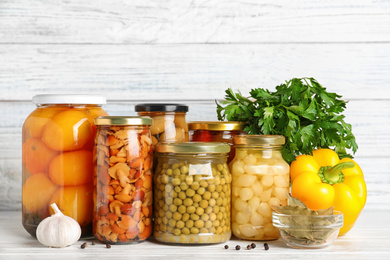 Glass jars with different pickled vegetables on white wooden table