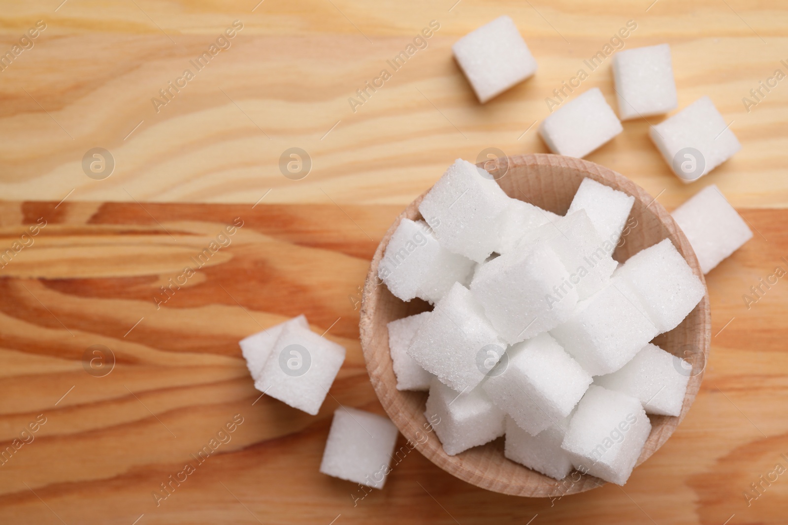 Photo of White sugar cubes in bowl on wooden table, top view. Space for text