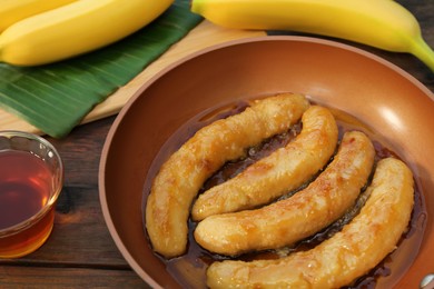 Photo of Delicious fresh and fried bananas with rum on wooden table, closeup