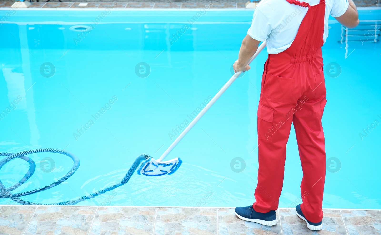 Photo of Male worker cleaning outdoor pool with underwater vacuum