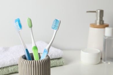 Photo of Plastic toothbrushes in holder, towels and cosmetic products on white countertop, space for text