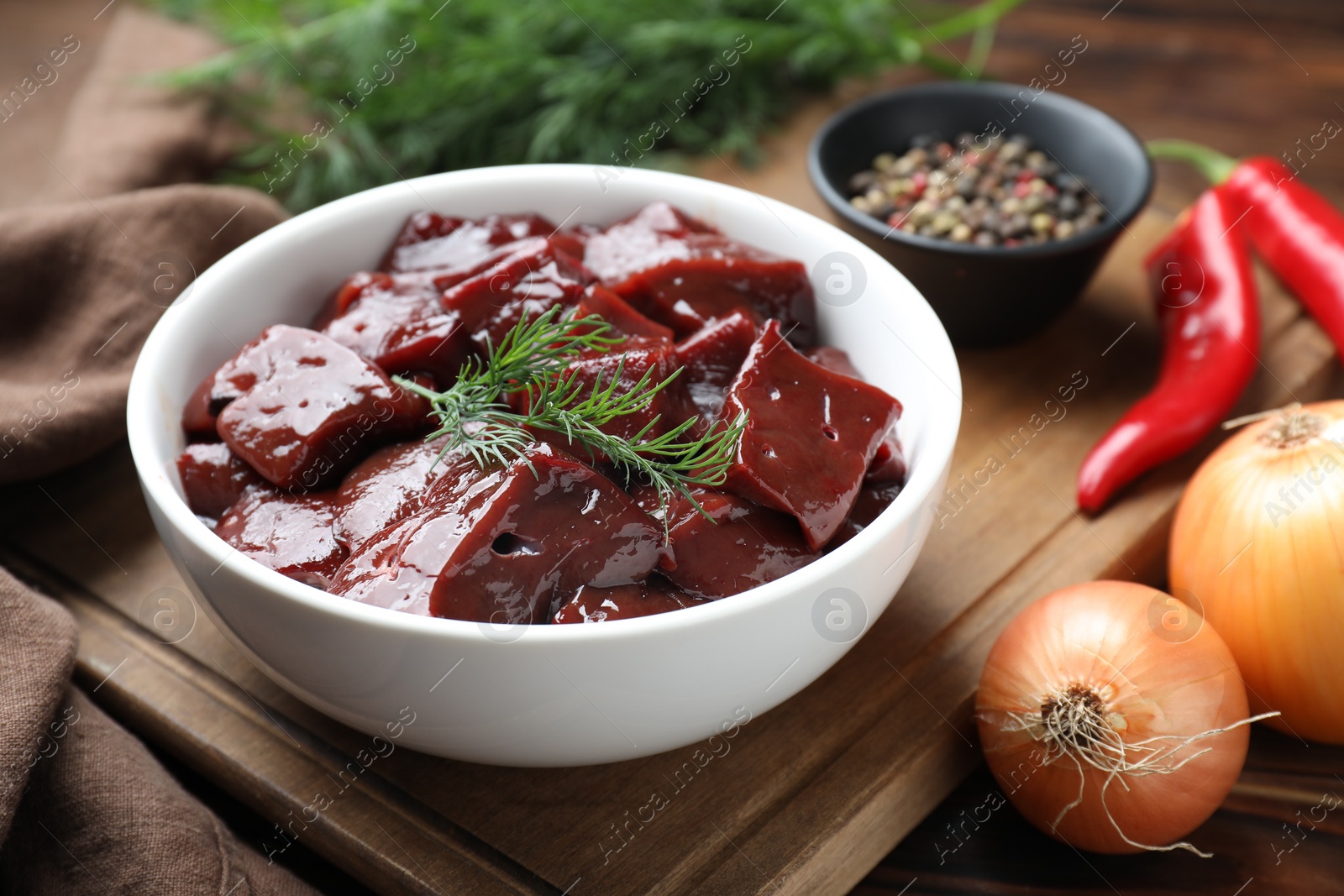 Photo of Cut raw beef liver with onions, spices, chili peppers and dill on wooden table