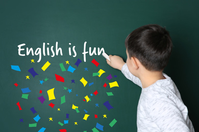 Image of Cute little boy writing ENGLISH IS FUN on chalkboard