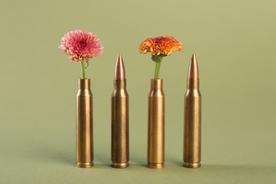 Photo of Bullets, cartridge cases and beautiful chrysanthemum flowers on olive background