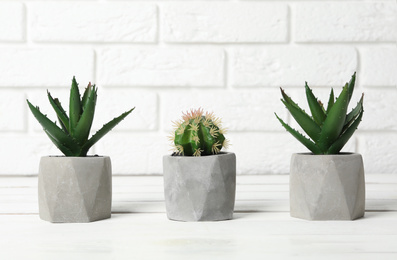 Photo of Beautiful artificial plants in flower pots on white wooden table near brick wall