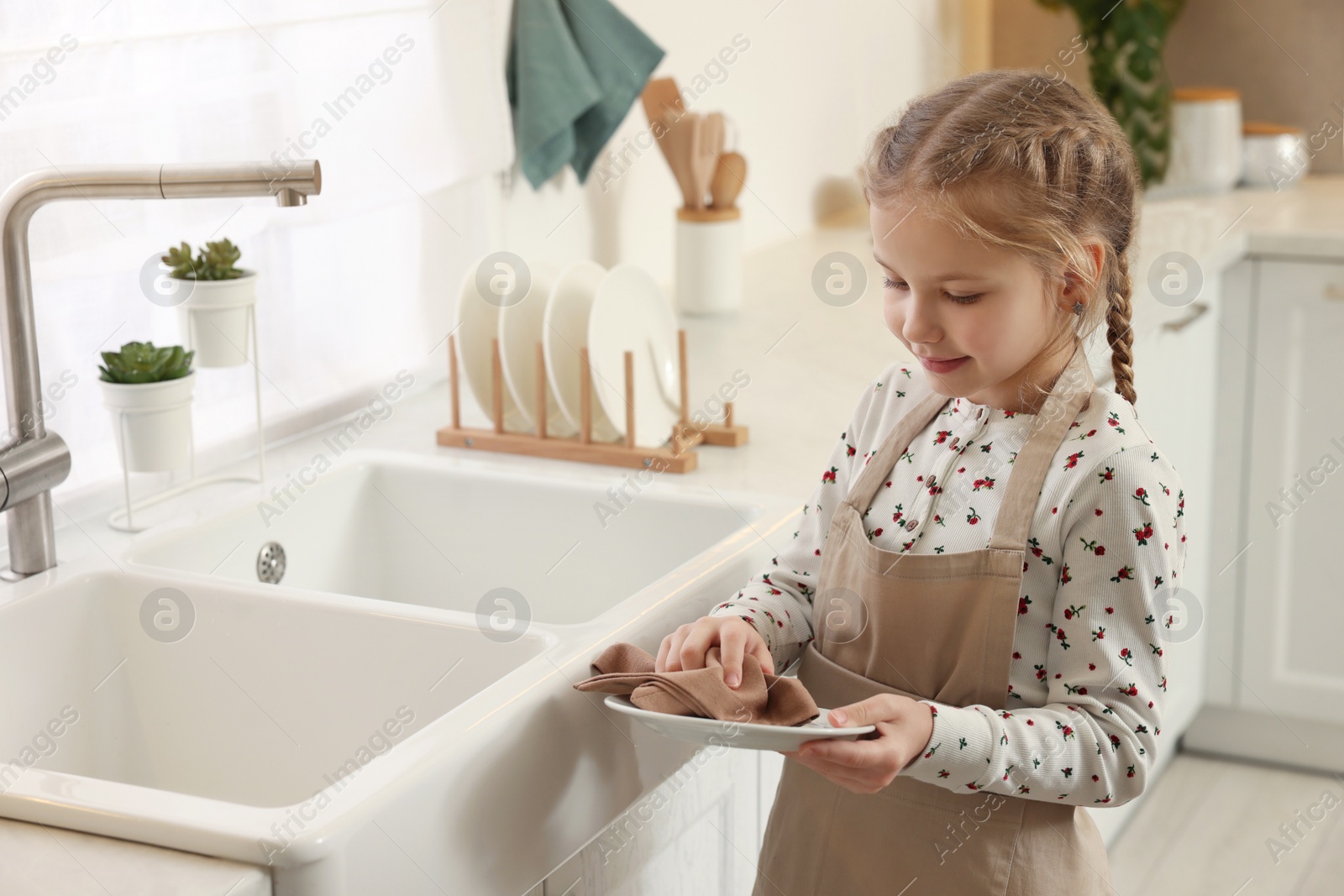 Photo of Little girl wiping plate with towel in kitchen