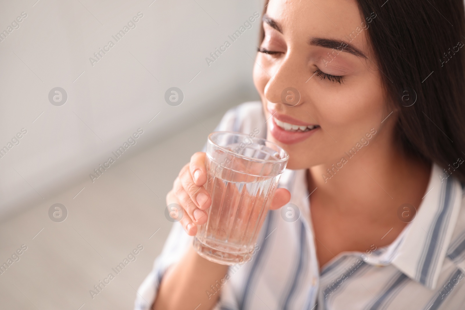 Photo of Young woman drinking pure water from glass indoors, closeup. Space for text
