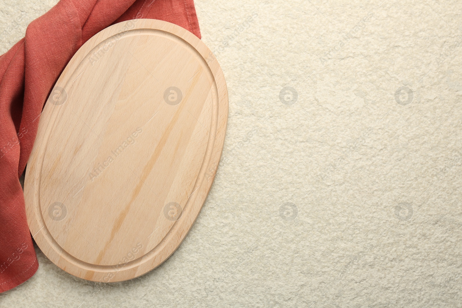 Photo of Wooden cutting board and cloth on beige table, top view. Space for text