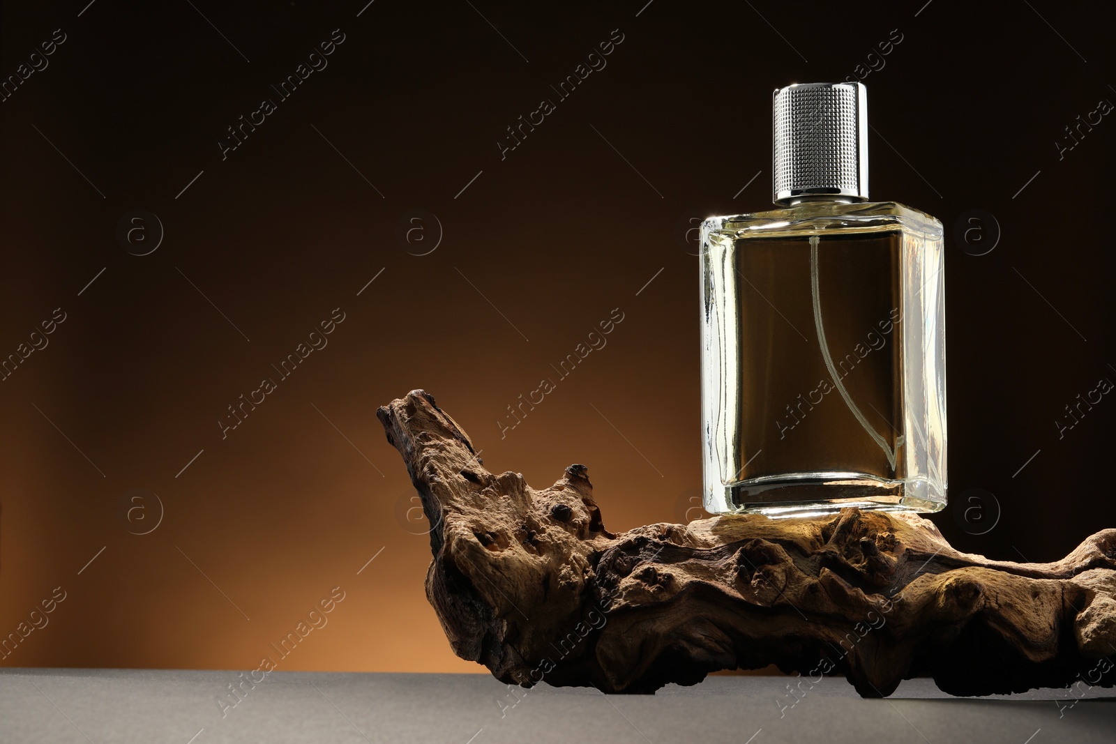 Photo of Luxury men`s perfume in bottle on grey table against brown background, space for text