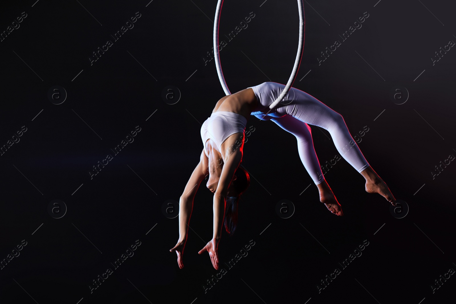 Photo of Young woman performing acrobatic element on aerial ring indoors