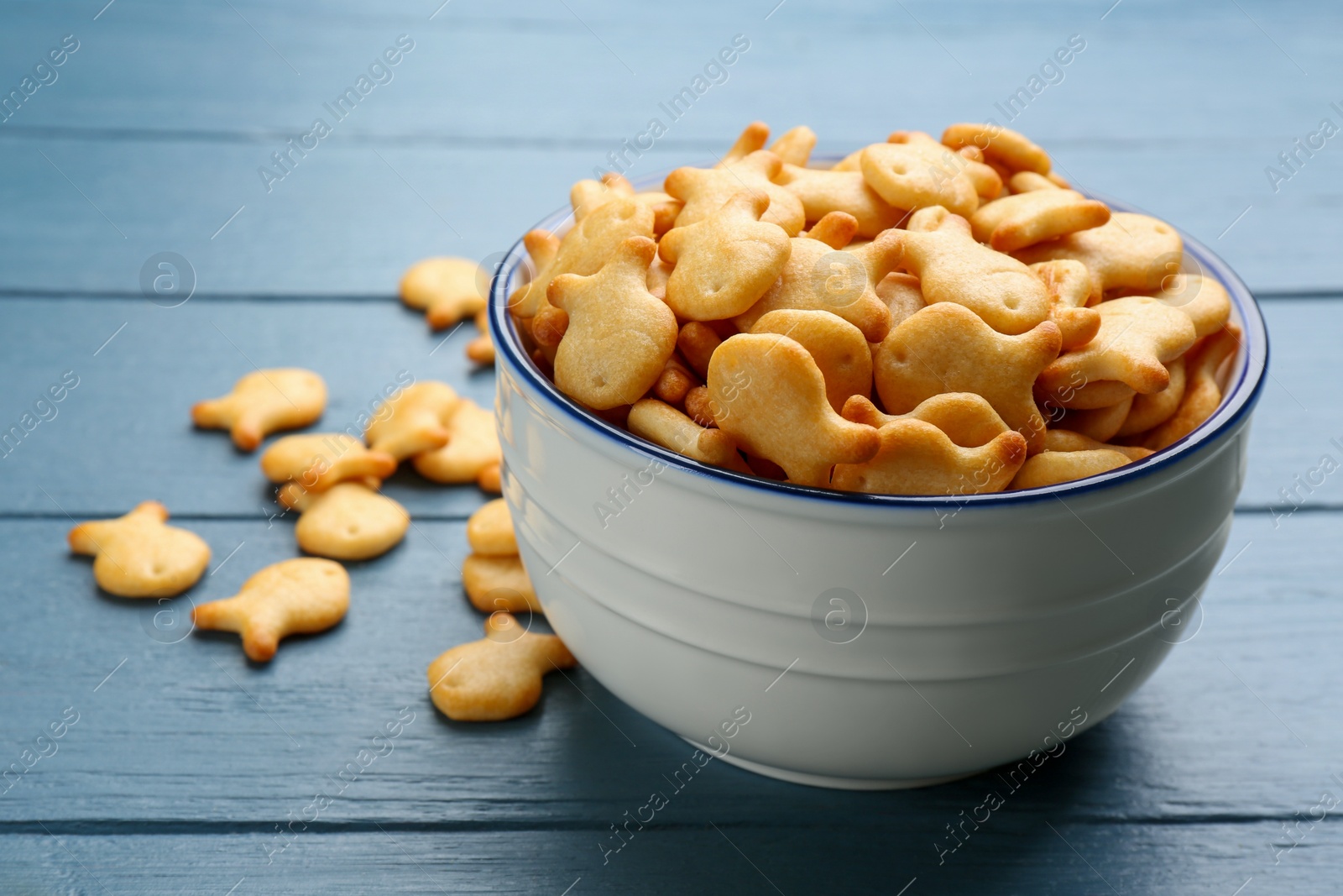 Photo of Delicious goldfish crackers in bowl on blue wooden table