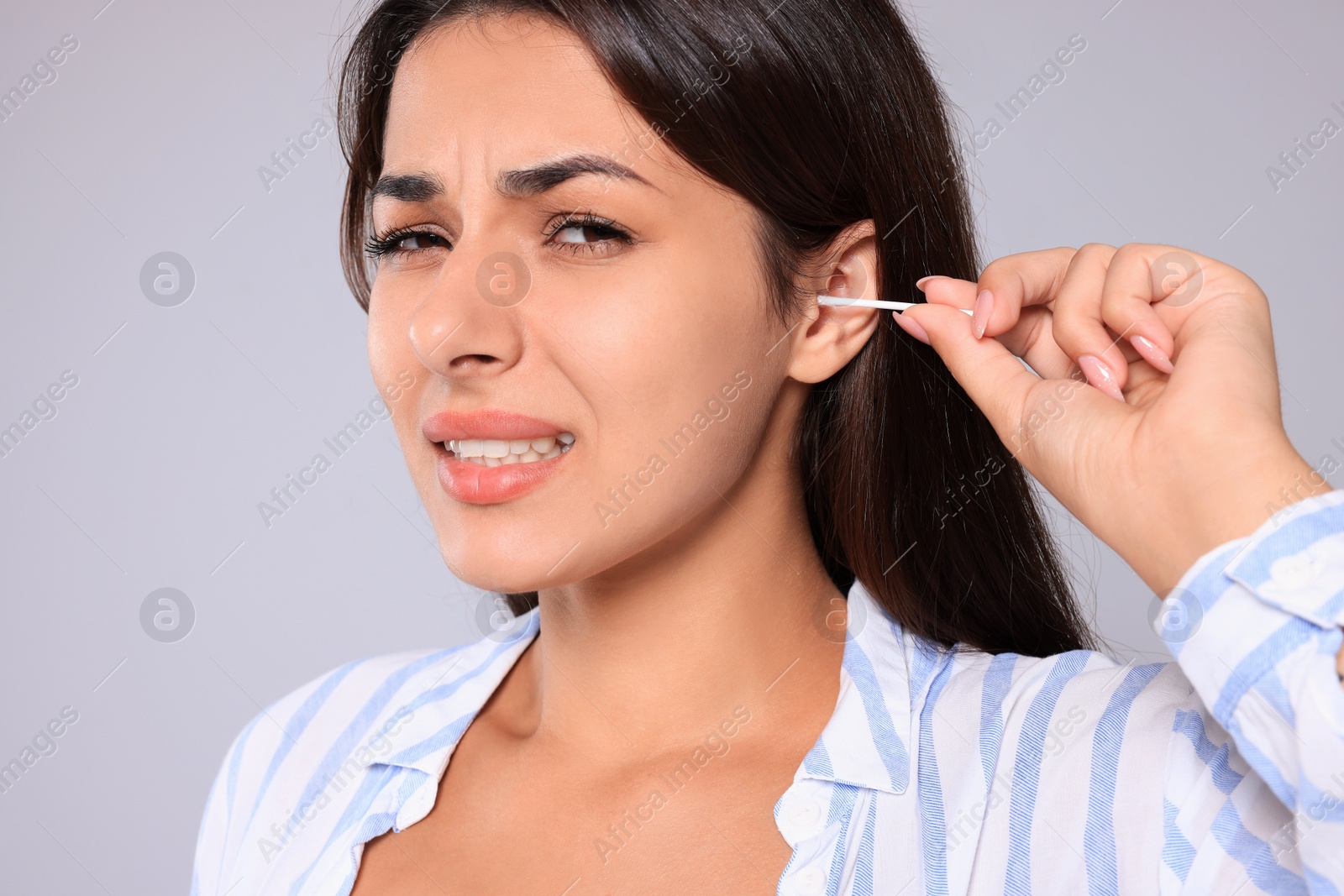 Photo of Young woman cleaning ear with cotton swab on light grey background, closeup