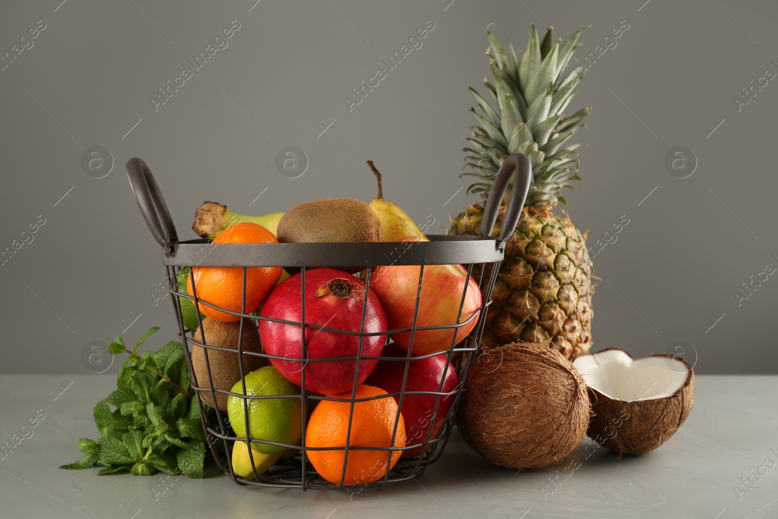 Photo of Metal basket and different ripe fruits on grey table