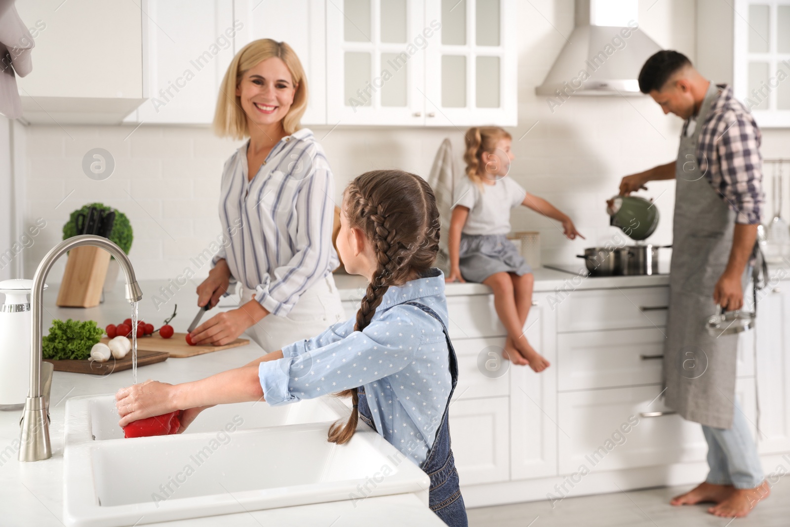 Photo of Little girl with her mother washing vegetables together in modern kitchen