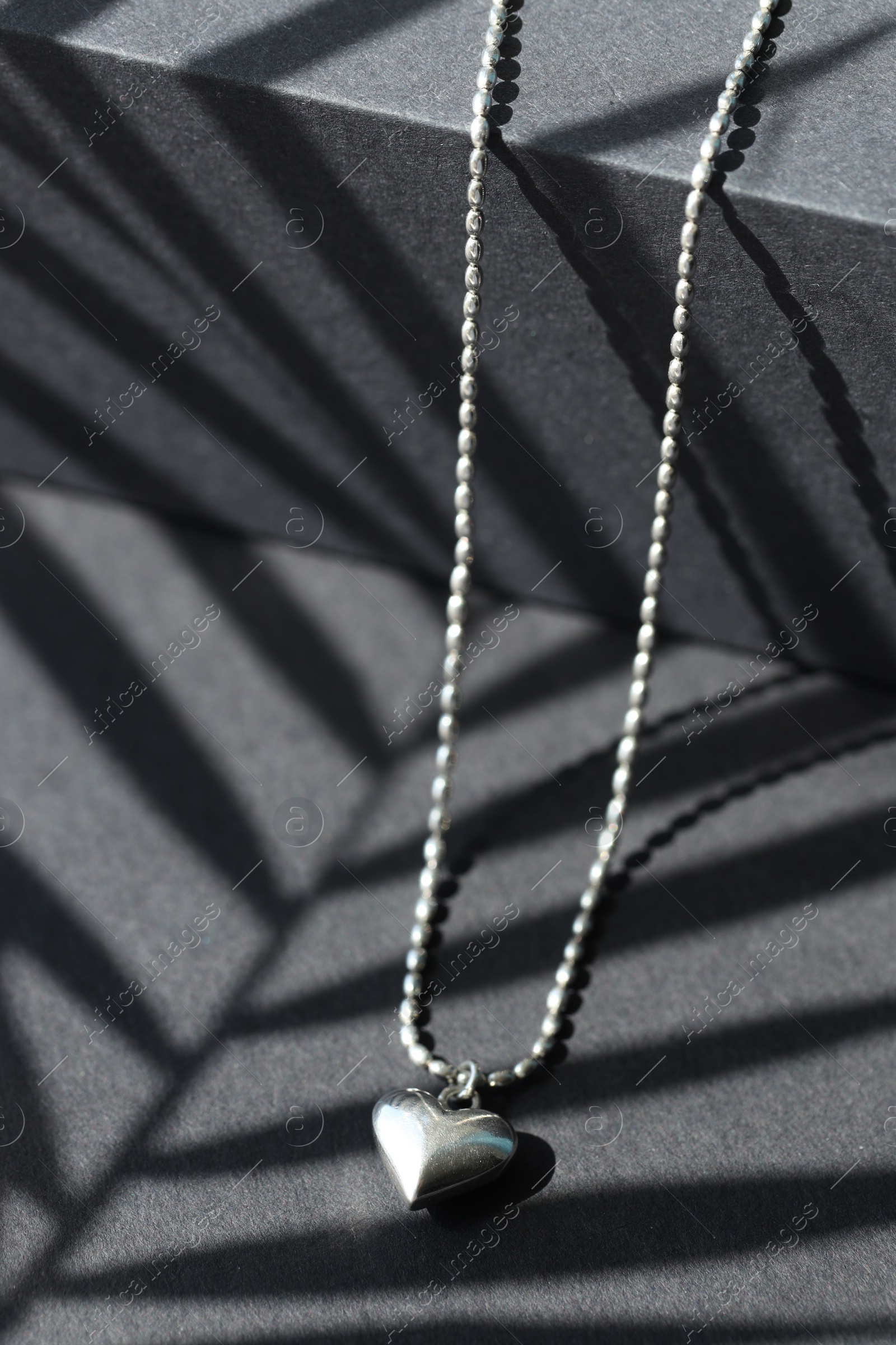 Photo of Metal chain with pendant on black table, closeup. Luxury jewelry