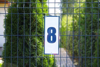 Photo of Plate with house number eight hanging on iron fence outdoors