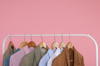 Rack with stylish clothes on wooden hangers against pink background, space for text