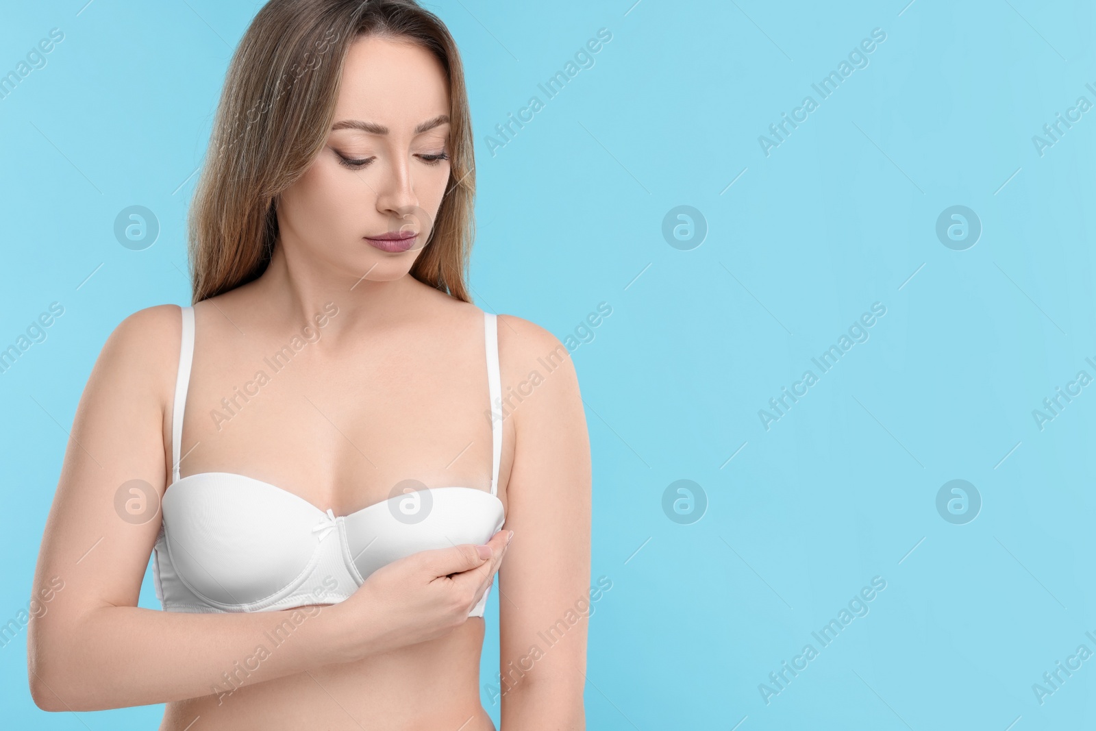 Photo of Mammology. Young woman doing breast self-examination on light blue background, space for text