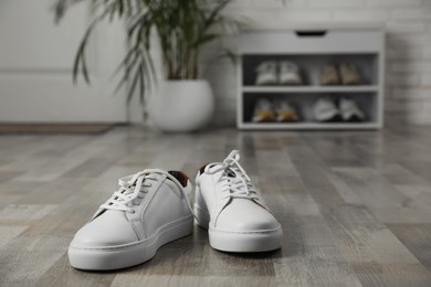 Photo of Pair of stylish white sneakers on floor in hallway, space for text
