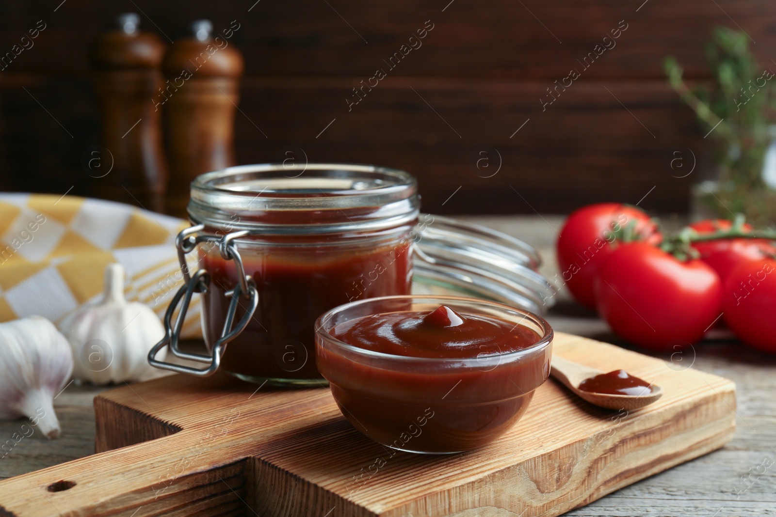 Photo of Tasty barbeque sauce in bowl, jar and spoon on wooden table, closeup