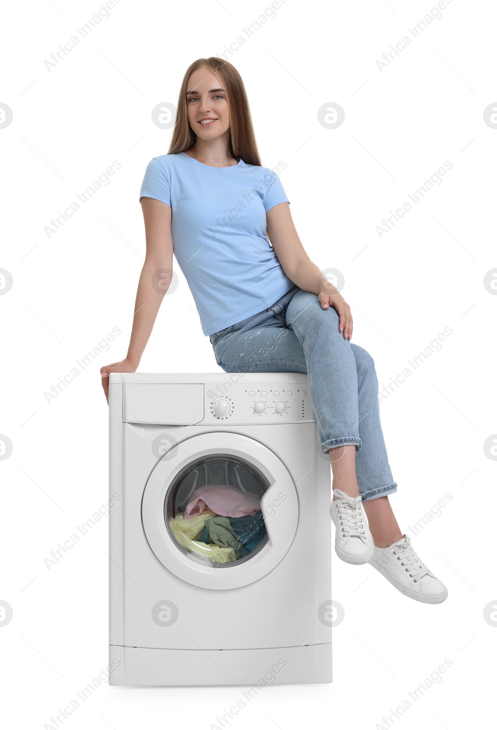 Photo of Beautiful young woman on washing machine with laundry against white background