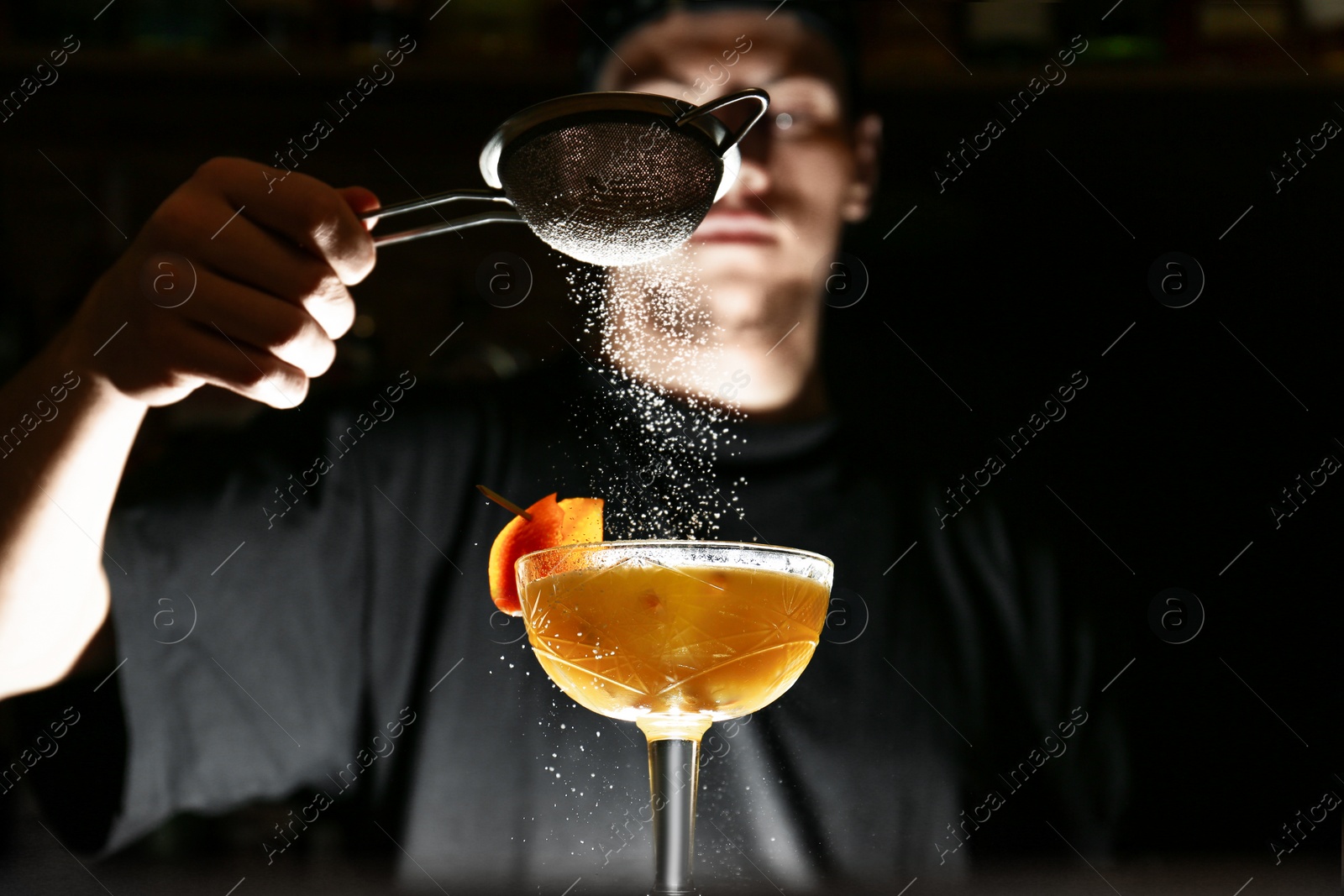 Photo of Bartender decorating fresh alcoholic cocktail in bar, focus on glass