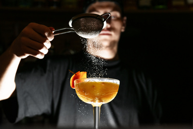 Bartender decorating fresh alcoholic cocktail in bar, focus on glass