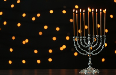 Photo of Hanukkah menorah with candles on table against blurred lights