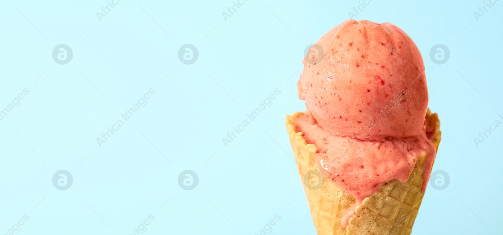 Photo of Delicious pink ice cream in waffle cone on light blue background, closeup. Space for text