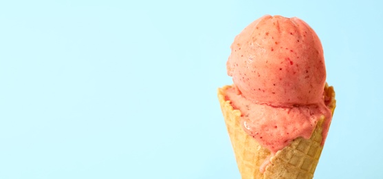 Photo of Delicious pink ice cream in waffle cone on light blue background, closeup. Space for text