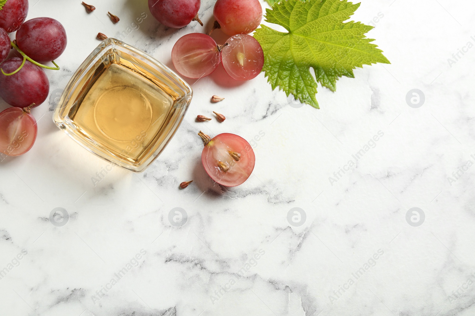 Photo of Bowl of natural grape seed oil on white marble table, flat lay with space for text. Organic cosmetic