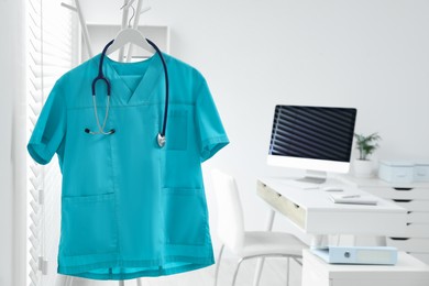 Photo of Turquoise medical uniform and stethoscope hanging on rack in clinic. Space for text
