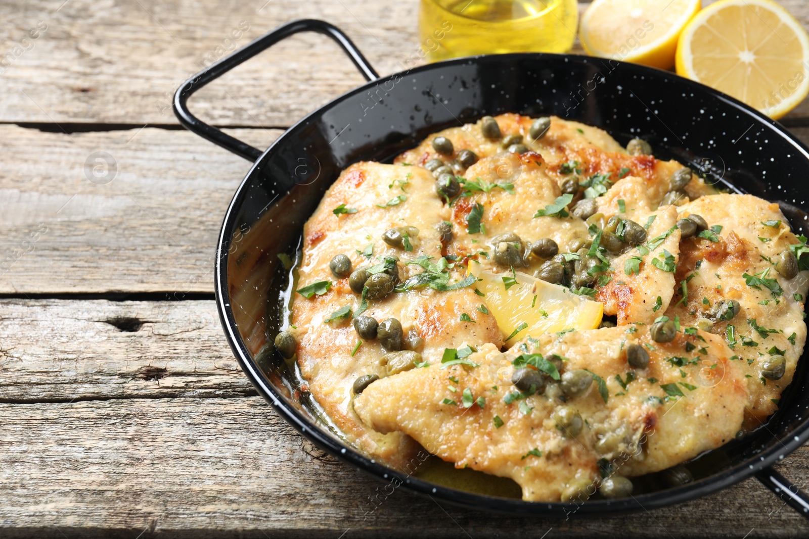 Photo of Delicious chicken piccata with herbs on wooden table. Space for text