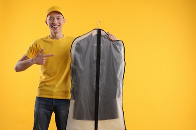 Photo of Dry-cleaning delivery. Happy courier holding garment cover with clothes on orange background, space for text