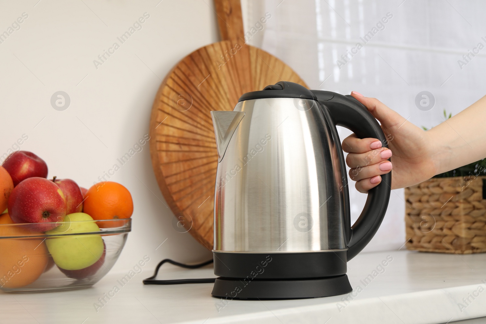 Photo of Woman with electric kettle in kitchen, closeup