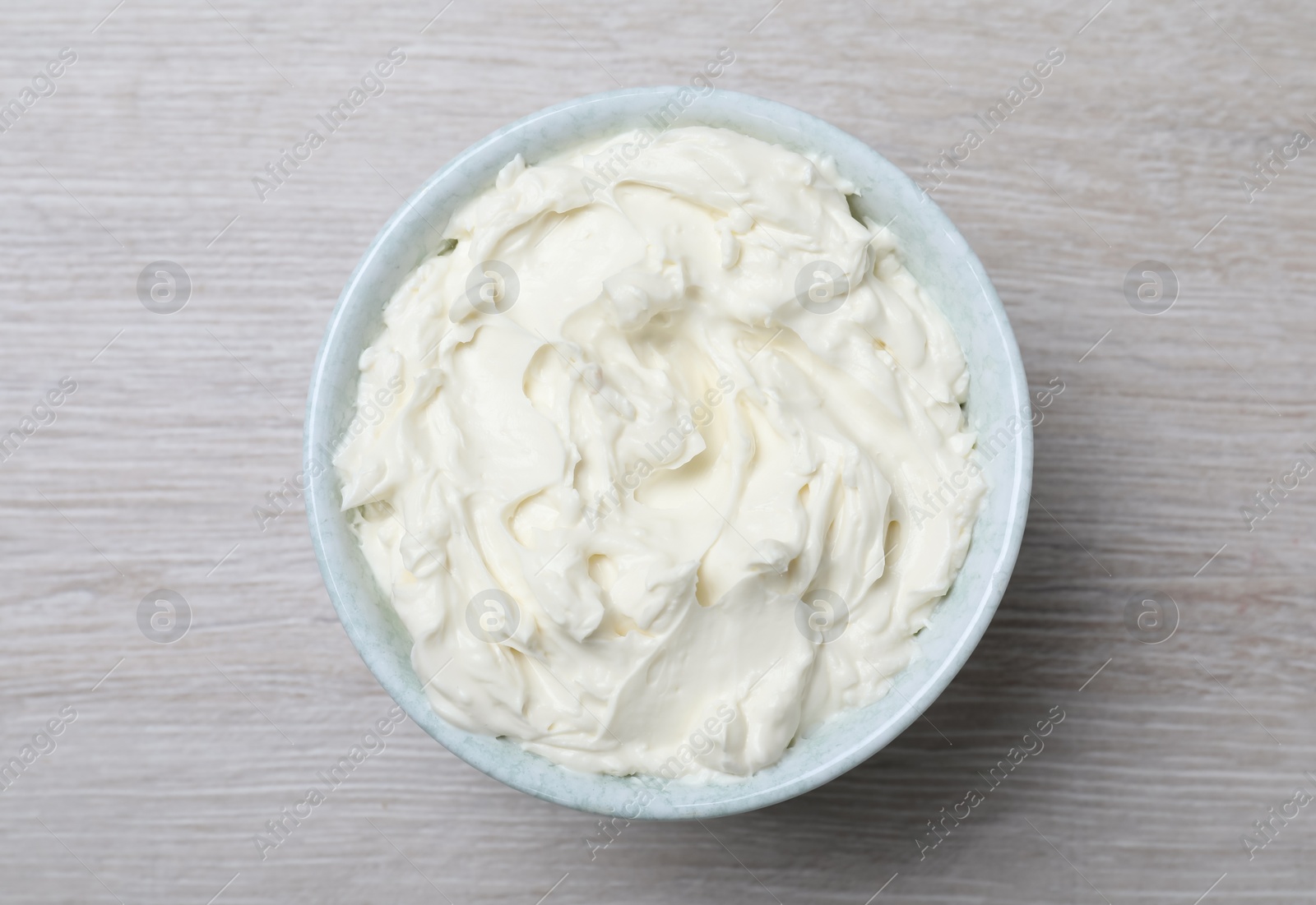 Photo of Bowl of tasty cream cheese on white wooden table, top view