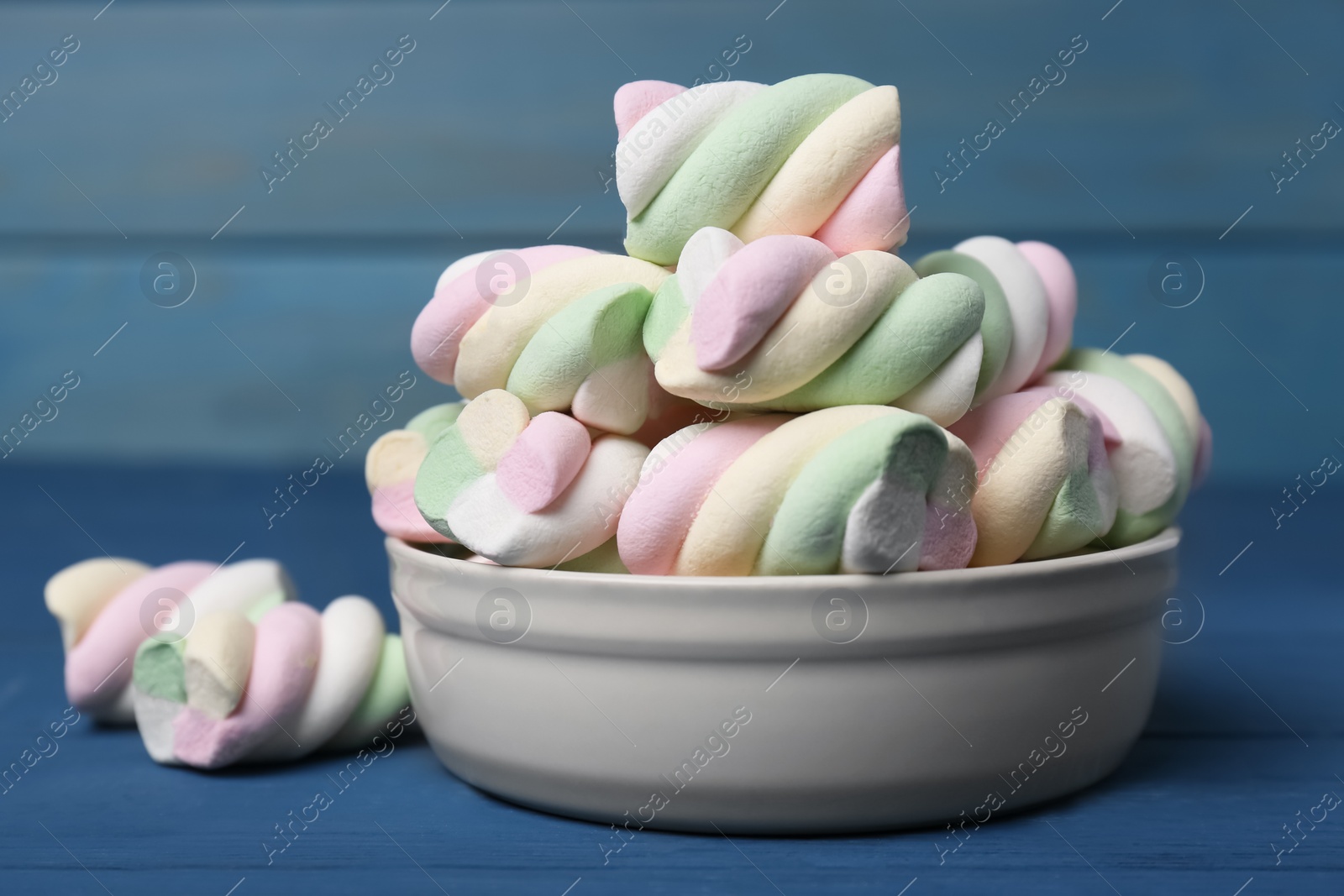 Photo of Bowl with colorful marshmallows on blue wooden table, closeup