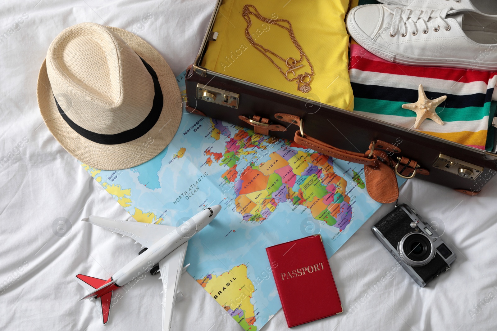 Photo of Packed suitcase and travel accessories on white fabric, above view. Summer vacation