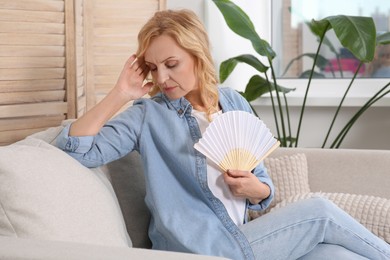 Woman waving hand fan to cool herself at home. Hormonal disorders