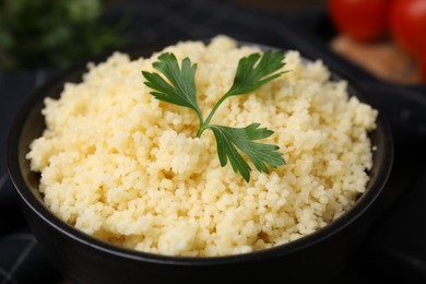 Tasty couscous and fresh parsley in bowl on table, closeup