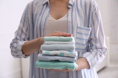 Photo of Woman holding stack of baby's clothes indoors, closeup