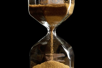 Photo of Hourglass with flowing sand on dark background. Time management