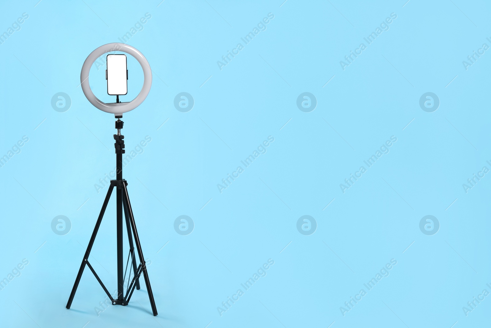 Photo of Modern tripod with ring light and smartphone on light blue background. Space for text