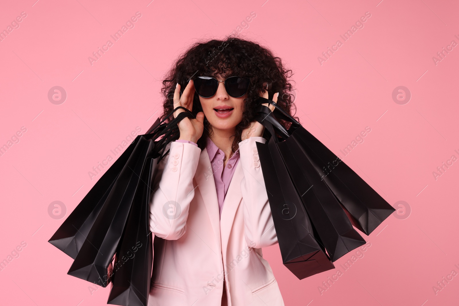 Photo of Happy young woman with shopping bags and stylish sunglasses on pink background