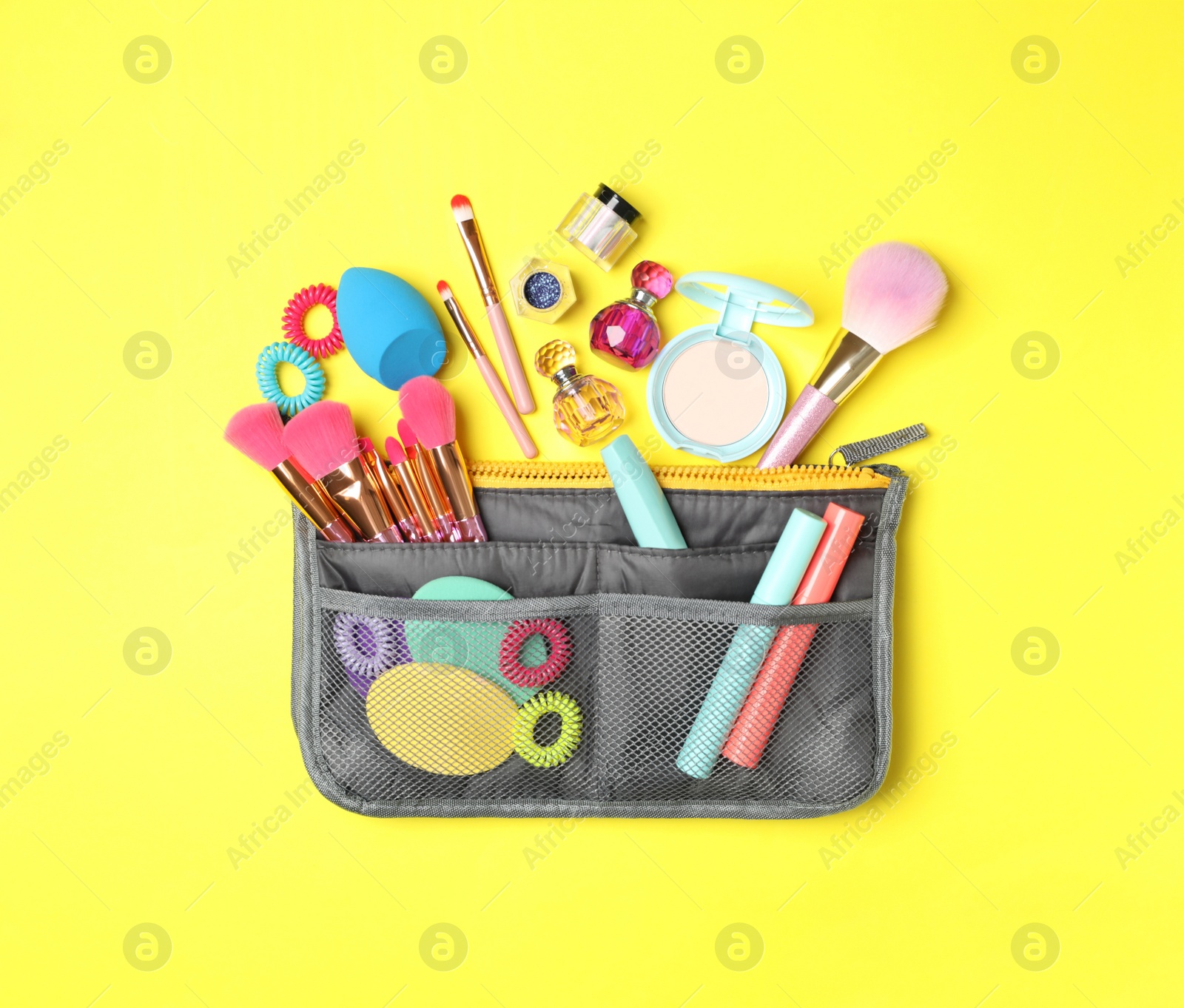 Photo of Cosmetic bag with makeup products and beauty accessories on yellow background, flat lay