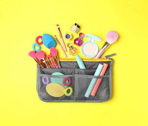 Photo of Cosmetic bag with makeup products and beauty accessories on yellow background, flat lay
