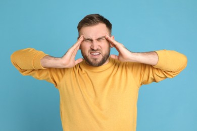 Man suffering from migraine on light blue background